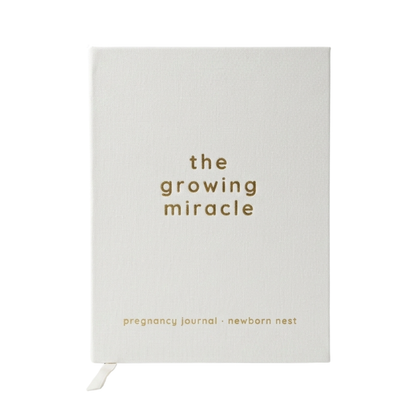 A white hardcover pregnancy journal with gold text reading 'the growing miracle' and 'pregnancy journal - newborn nest' on a clean white background.